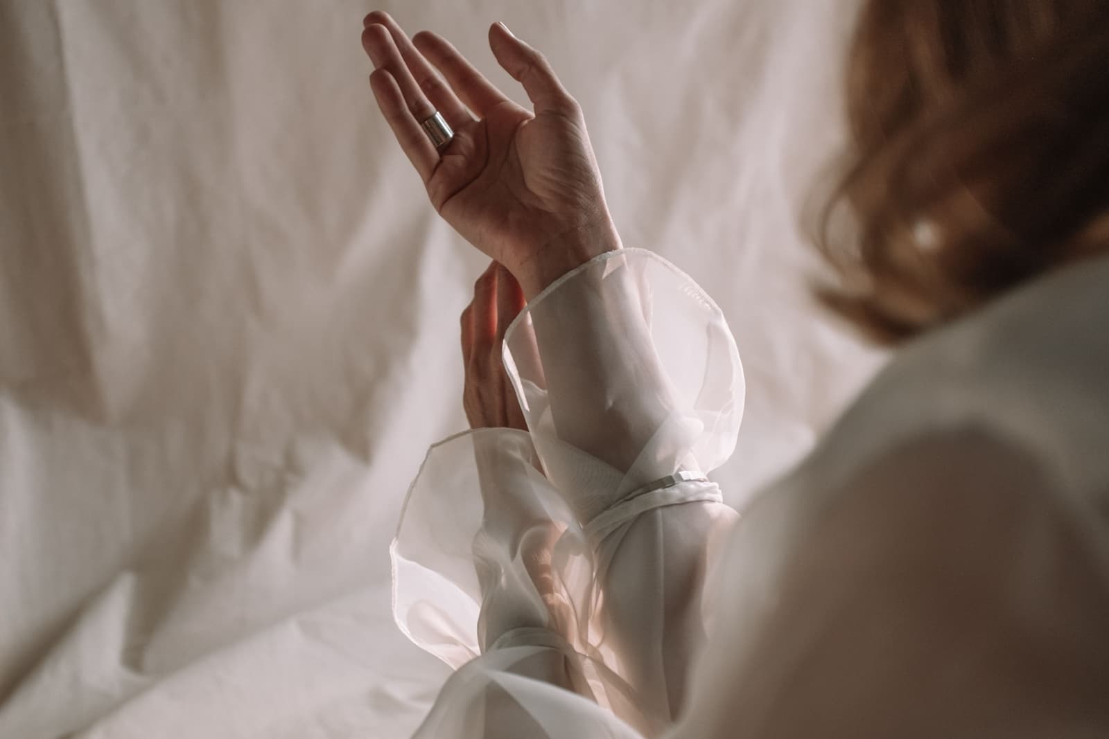 A bride's raised hand in a sheer white sleeve, against soft draped linen
