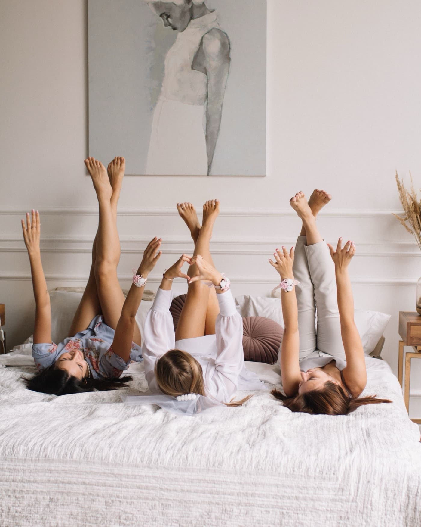 Three women lying back on a bed with legs and arms raised, matching floral wrist ties